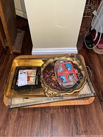 Photo of stacked trays and dishes showing various trays including a large decorative floral tray and square trivets with fruit and wine themes.
