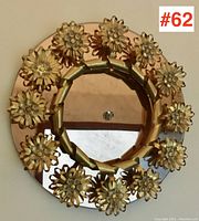 Front view of round peach glass mirror with 12 gilt brass floral decorations embellished with crystals arranged around inner and outer circle.