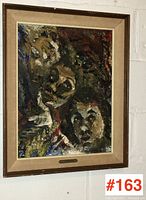 Framed abstract expressionist painting featuring three faces. Visible textured brushwork in dark tones. Beige linen mat and wooden frame.