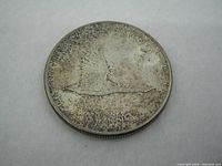 Obverse of the 1967 Canada Silver Dollar coin showing a flying goose in flight across a water background with the inscription 'DOLLAR' at the bottom edge.