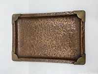Top view of rectangular copper tray with four brass corner protectors, showing hammered surface texture and patina.