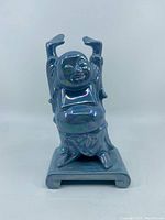 Front view of the blue lustre ceramic Buddha figure showing the glossy iridescent finish and joyful pose.