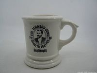Front side of the white ceramic shaving mug showing the black print design and handle.
