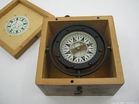 Open wooden box showing the black metal mounted compass inside with clear directional dial.