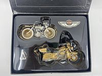 Photo of the two Harley Davidson motorcycle ornaments and emblem in original molded plastic packaging inside the box.