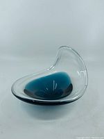 Angled side view of a clear glass dish with a blue center, showing the overall shape and smooth surface.