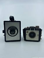 Two vintage cameras, Kodak Brownie Holiday Flash and Ansco Shur-Flash side by side, showing front faces.