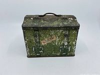 Front and handle of green metal biscuit tin shaped like luggage showing wear and paint loss.