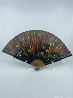 Front view of the vintage folding hand fan showing hand painted floral designs on dark fabric and wooden ribs.