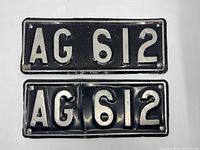 Top side of front showing both matching black license plates with raised white letters AG 612, one plate dented and worn.