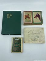 Four vintage playing card sets in their original boxes: green 'How to Deal with Cards', white 'Chippendale', box with horse illustrations, and green 'Golden Nugget'.