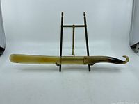 Full view of the vintage page turner with horn handle placed on a stand against a white background.