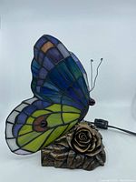 Side view of the butterfly table lamp showing stained glass wings and bronze-tone rose base with power cord.
