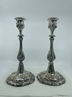 Front view of the pair of silver plated candlesticks standing upright showing detailed floral designs and scalloped bases.