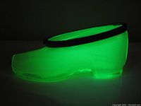 Uranium glass shoe glowing bright green under UV light, showing translucency and color.