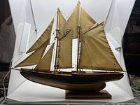 Side view of the wooden model sailboat showing sails, rigging, and wooden stand