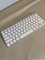 Apple Wireless Keyboard A1314 visible from an angle showing full keyboard layout with white keys and aluminum frame on a beige surface.