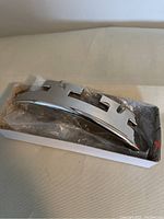 Polished chrome metal banjo rest with geometric cutout design in white box, front angle.