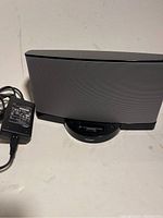 Bose SoundDock Series II speaker dock with power adapter placed on a white surface, showing front and side profile with cables.