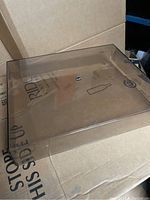 Clear plastic dust cover placed on cardboard with visible Dual brand sticker