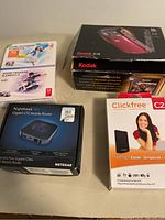Photo showing Kodak Z18 camera box, Adobe software boxes, Netgear Nighthawk router box, and Clickfree backup box.