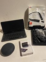 Google Nest Mini, Belkin iPad keyboard, LG Bluetooth earphones with packaging, and Floral Beauty UV sterilizer box shown together.