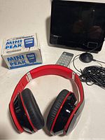 Photo showing Mini Peak charger box, portable HD TV on stand, remote, and red/black over-ear headphones.
