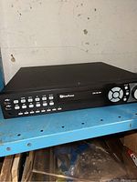 Full view of the Everfocus DVR unit showing front panel buttons, control dial, display, and branding on a blue shelf.