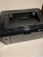 Front and top view of the HP LaserJet P1102w printer showing output tray and control buttons.