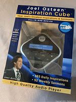 Front view of the Joel Osteen Inspirational Cube in original packaging showing the cube audio player inside with the display screen and control buttons visible.