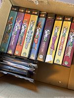 Photo showing 10 The Sims 2 PC game titles in their cases inside a box. Titles include base game, Nightlife, Bon Voyage, Pets, University, Open for Business expansions and Family Fun Stuff pack among others.