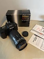 Nikon N90s camera with attached Nikkor 70-210mm f/4 lens next to box and manuals.