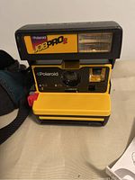 Front view of Polaroid Job Pro 2 camera showing yellow and black body, lens, flash head, and branding.