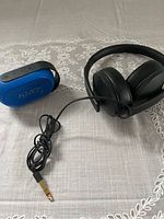 Sennheiser black wired headphones with cushioned ear cups and 3.5mm gold-plated audio jack next to blue Auvio Bluetooth speaker with black strap and control buttons.
