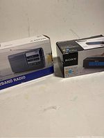 Photo showing boxed Sony IF-38 FM/AM 2-band radio and Sony ICF-C707 Dream Machine clock radio side by side on a white surface.