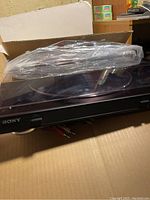 Sony PS-LX300USB USB Stereo Turntable on cardboard with dust cover wrapped in plastic, showing the front with Sony branding.