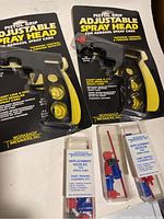 Two black and yellow pistol grip adjustable spray heads in original packaging along with two sets of replacement nozzles and spray tubes in clear plastic boxes.
