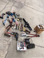 Overview of all miscellaneous tools including electric chainsaw, drill, saws, and clamps spread on pavement