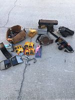 Power tools including a belt sander, circular saw, drill, and Skil saw with assorted drill bit sets and accessories arranged on the ground.