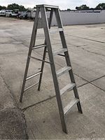 A full view of an aluminum A-frame ladder standing on a concrete surface showing six steps on one side and a top platform step.