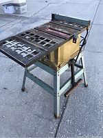 Front side view showing the saw table with slots and metal stand with rust and wear.