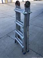 Side view of folded aluminum ladder showing steps, rubber feet, and pulley wheels with rust.