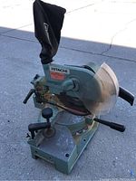 Front-side view of Hitachi chop saw, showing circular blade, dust bag, and base with adjustment knobs.