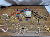 Full lot spread of costume jewelry including watches, beads, pins, bracelets, rings and pendants on wood surface