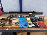 Wide shot of the entire lot on wooden workbench showing multiple tools including pneumatic wrench, soldering station, Dremel drills, Dewalt sander, bit sets and other tools
