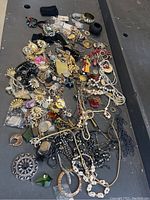 Overview of all miscellaneous costume jewelry spread out on a black surface showing diverse pieces including necklaces, bracelets, pendants, and brooches.