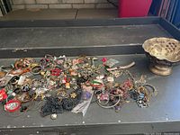 Lot of assorted costume and semi-precious jewelry spread out alongside a hammered silver plated bowl with embossed floral and grape designs.