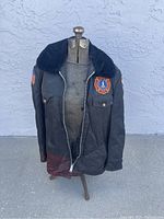 Front view of vintage NASA fire services jacket on dress form, showing faded black fabric and zipper issue.