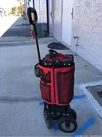 Folded red and black pop-out wagon by Ozark Trail with ergonomic black handle and mesh pockets, wheels visible at bottom.