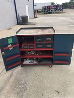 Front view of rolling metal toolbox workbench with open doors, showing drawers and storage compartments filled with various small hand tools and items.